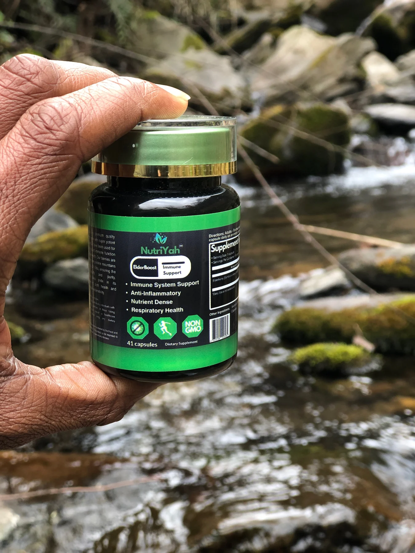 A hand holding ElderBoost beside a forest stream in St. Kitts